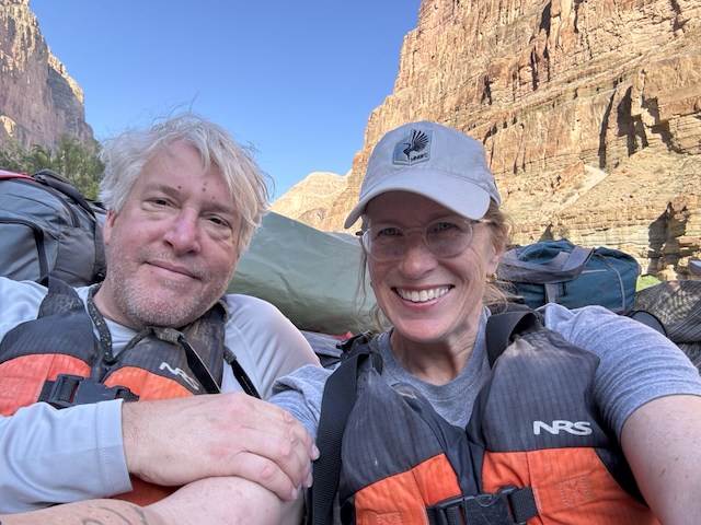 A smiling couple wearing PFDs with Grand Canyon as background